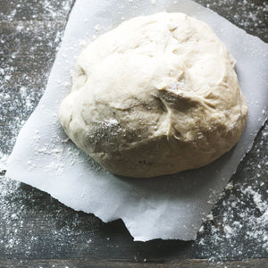 pizza dough on white parchment on a floured grey surface