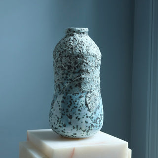 Speckled blue ceramic vase on a white pedestal against a gray background