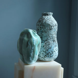 Two ceramic vases on a white pedestal against a dark blue wall