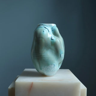 Greenish-blue ceramic vase on a white pedestal against a dark background