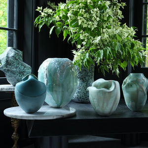 Collection of green ceramic vases on a table with a window in the background