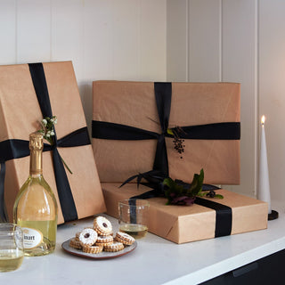 4 large presents elegantly wrapped in light brown tissue paper and tied with black silk ribbon, a small bough of privet tucked in the middle. A small terracotta, white-glazed dessert plate filled with Linzer Tarts and a two glasses of Ruinart Champagne with a grey candle glowing in the back. Enjoy.